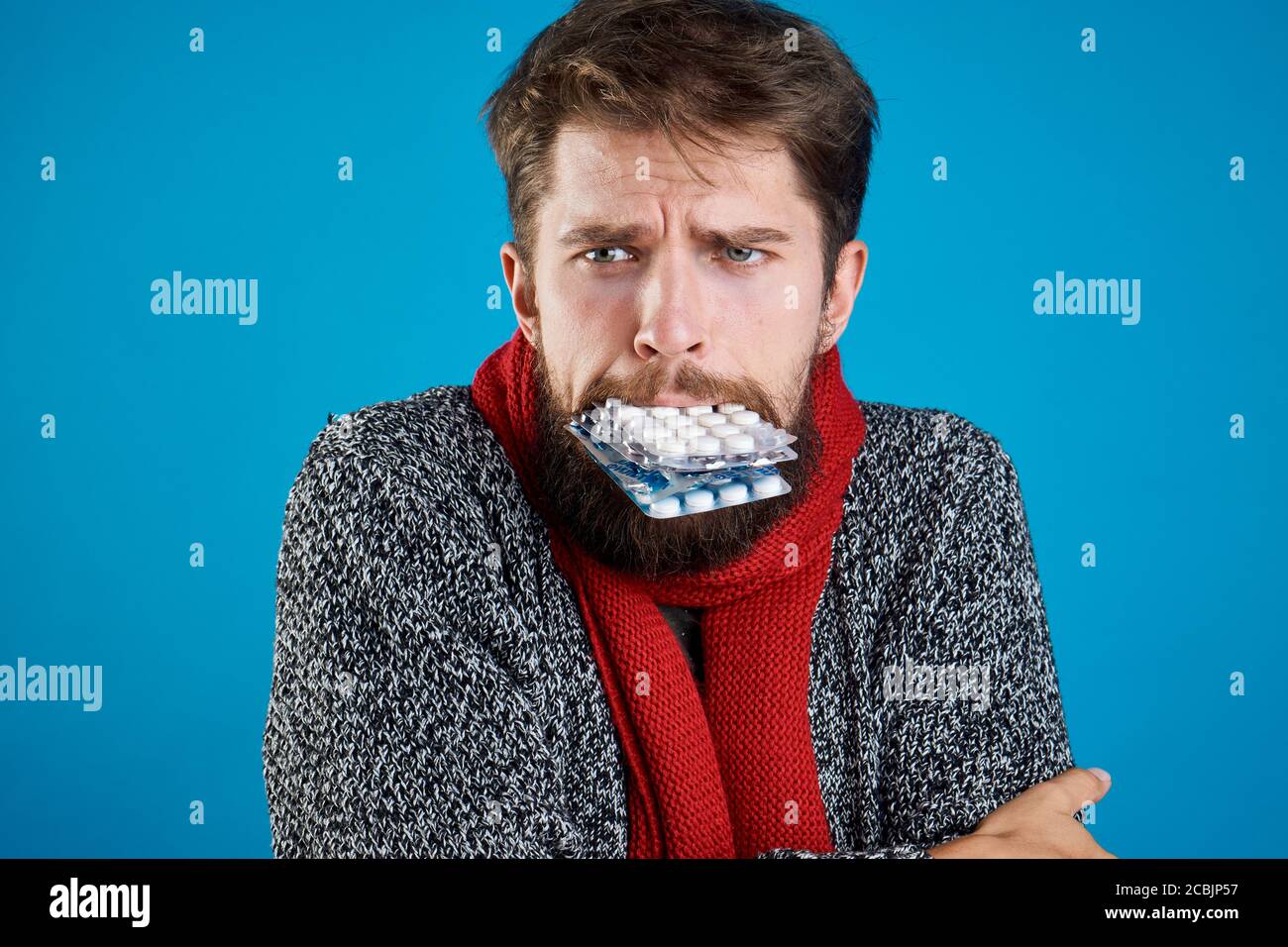 A man with pills in his teeth gestures with his hands health problems warm clothes red scarf Stock Photo