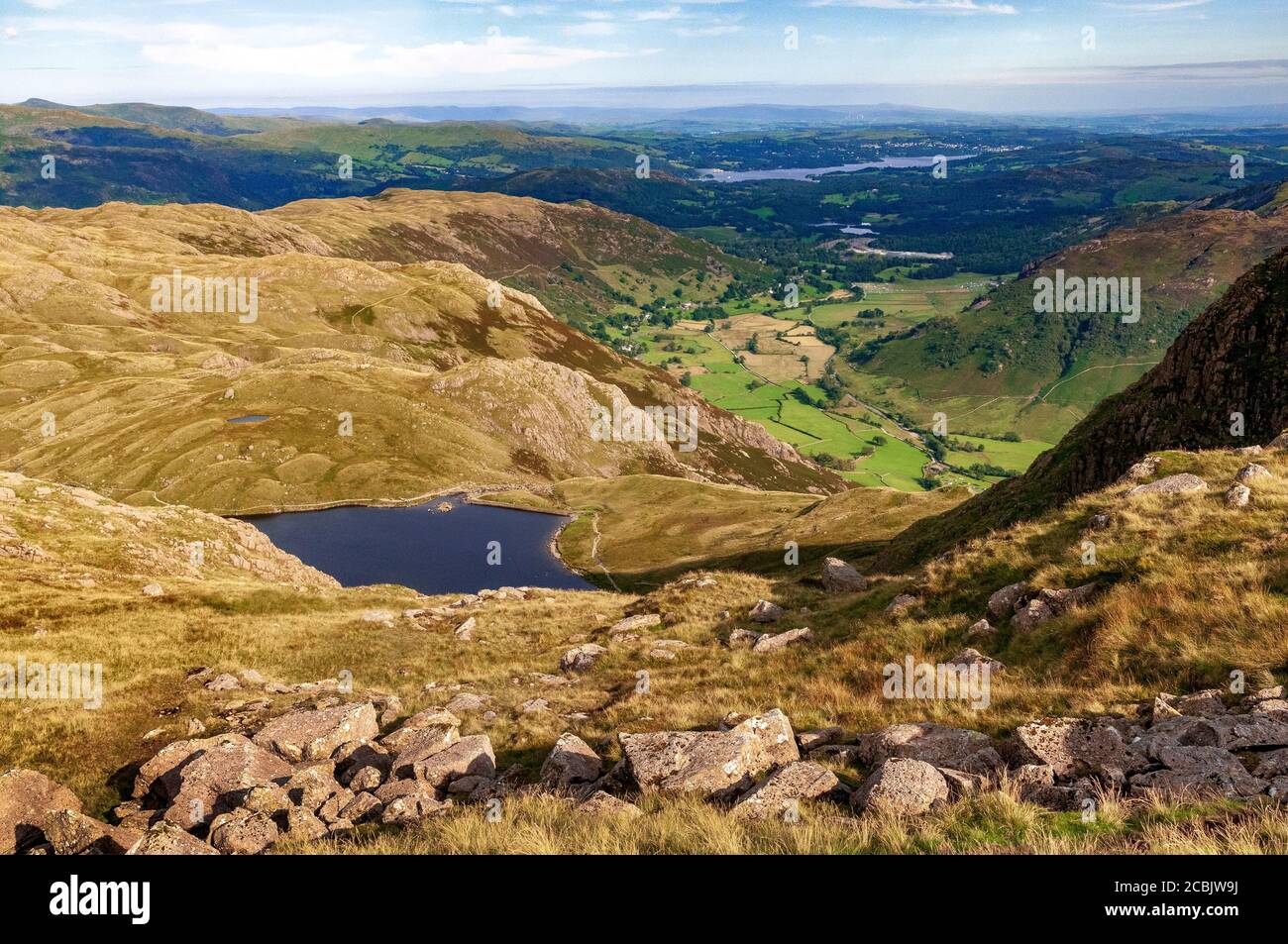Sticlke Tarn seen from Pavey Ark fell in the Langdales with the Langdale valley green fields and Lake Windermere in the distance. Stock Photo