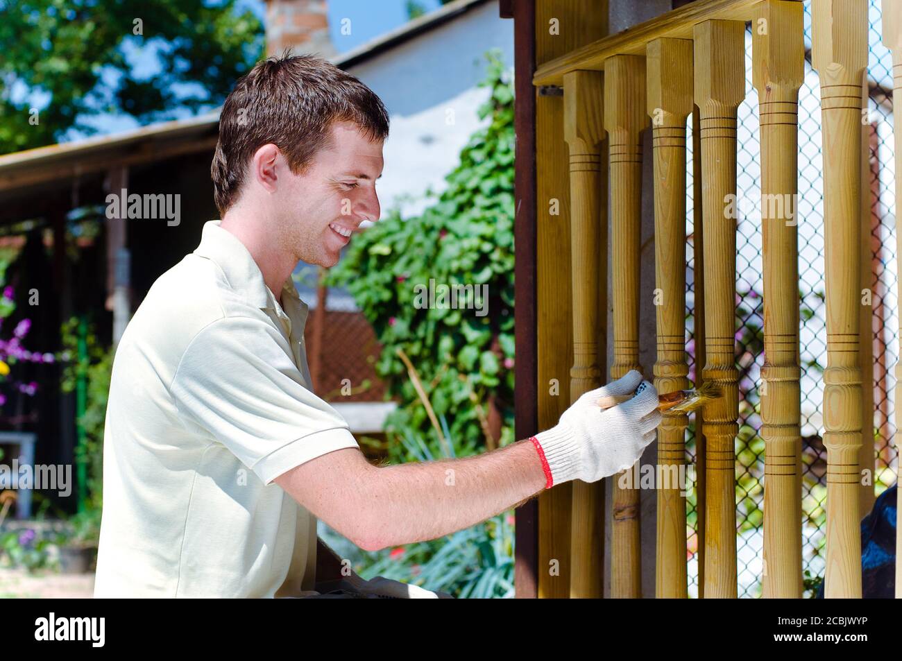 Young man painting wooden fence in the garden sitting near it Stock Photo