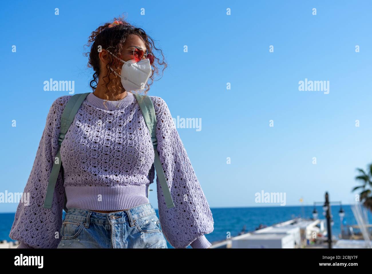 Portrait of an attractive young black woman walking with backpack and mask. Sightseeing Stock Photo