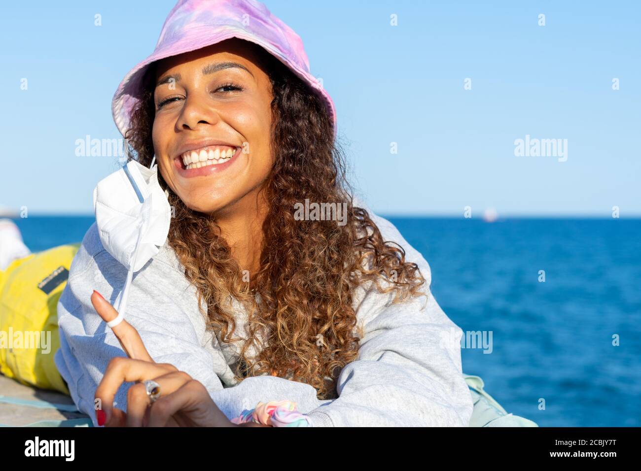 Portrait of an attractive young black woman lying relaxed on the beach with her mask off. Looking to the camera Stock Photo