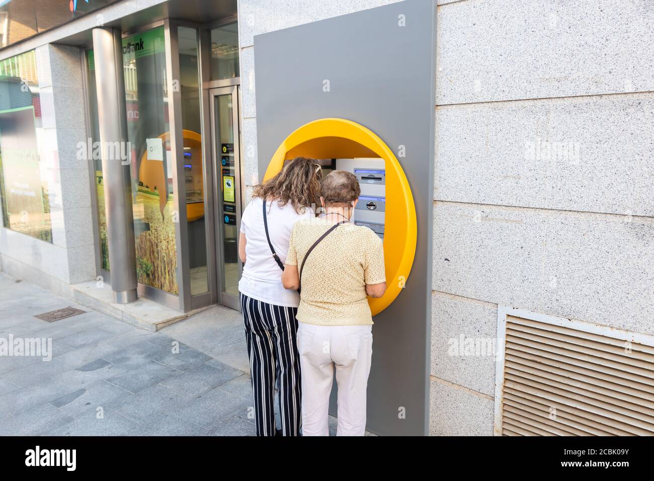 Huelva, Spain - August 13, 2020: Unidentified women using bank credit card in ATM machine is wearing a protective face mask due to covid-19 coronaviru Stock Photo