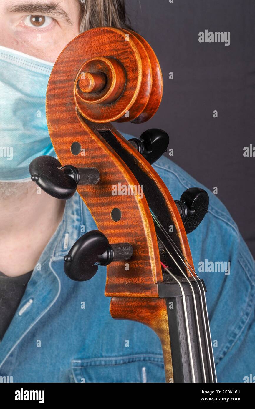 A vertical shot of a musician wearing a sanitary mask holding a cello ...