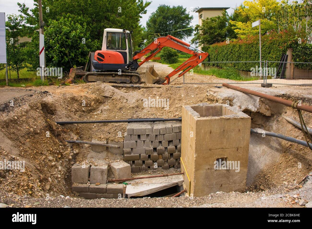 A sewer well trench & a compact crawler excavator with rotating house platform & continuous caterpillar track on a sewer replacement site in NE Italy Stock Photo