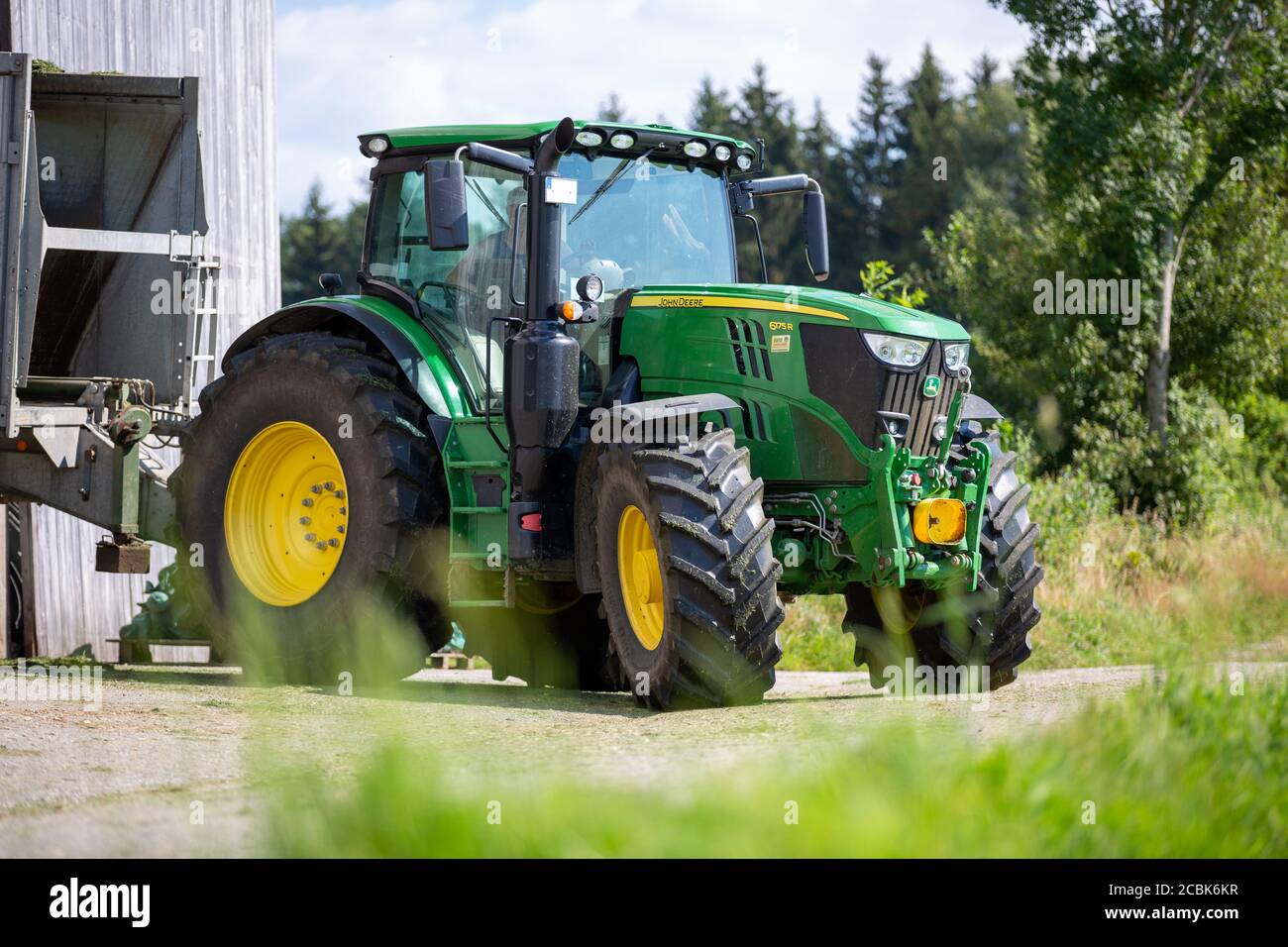 BAVARIA/ GERMANY - AUGUST 07,2020: John Deere 6175R tractor drives with a Fliegl Gigant trailer on a dirt road. Stock Photo