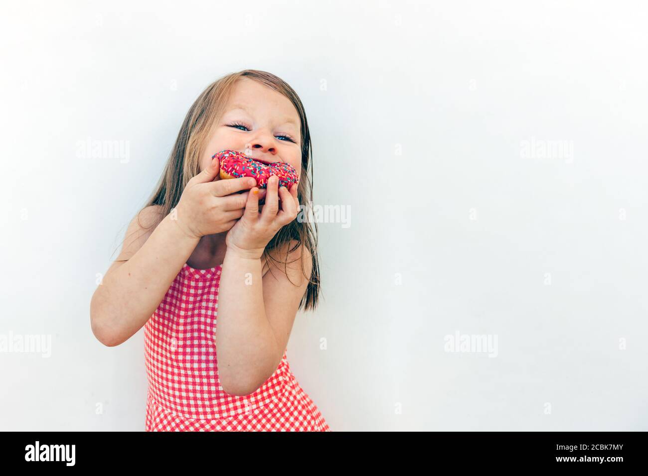 hungry happy girl eating donuts. kid holding donut with two hands against a white background Stock Photo