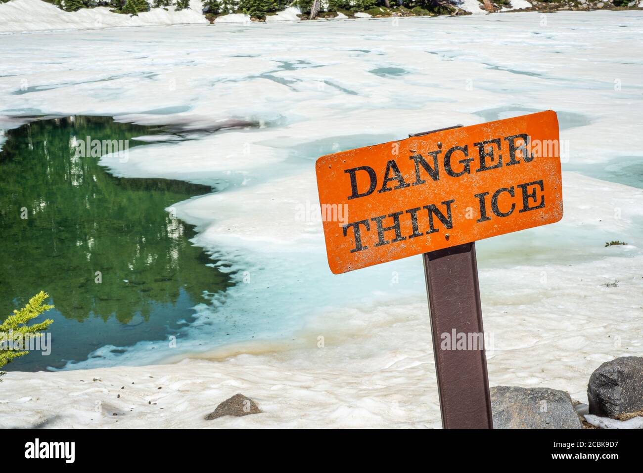 Thin ice warning notice on orange danger signboard by mountain lake Stock Photo