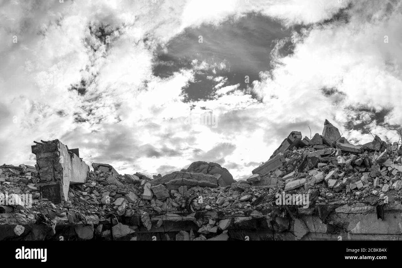 A pile of concrete gray debris of a destroyed building with a huge beam in the foreground against the background of a textured sky with clouds. Stock Photo