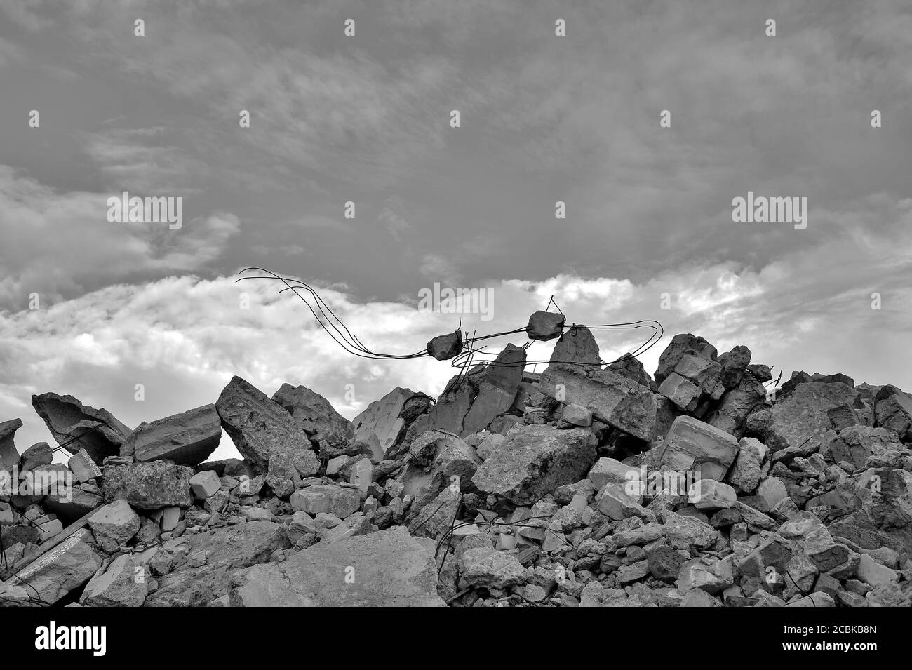 Concrete fragments of the remains of a destroyed building against the background of a textured sky with clouds. Stock Photo