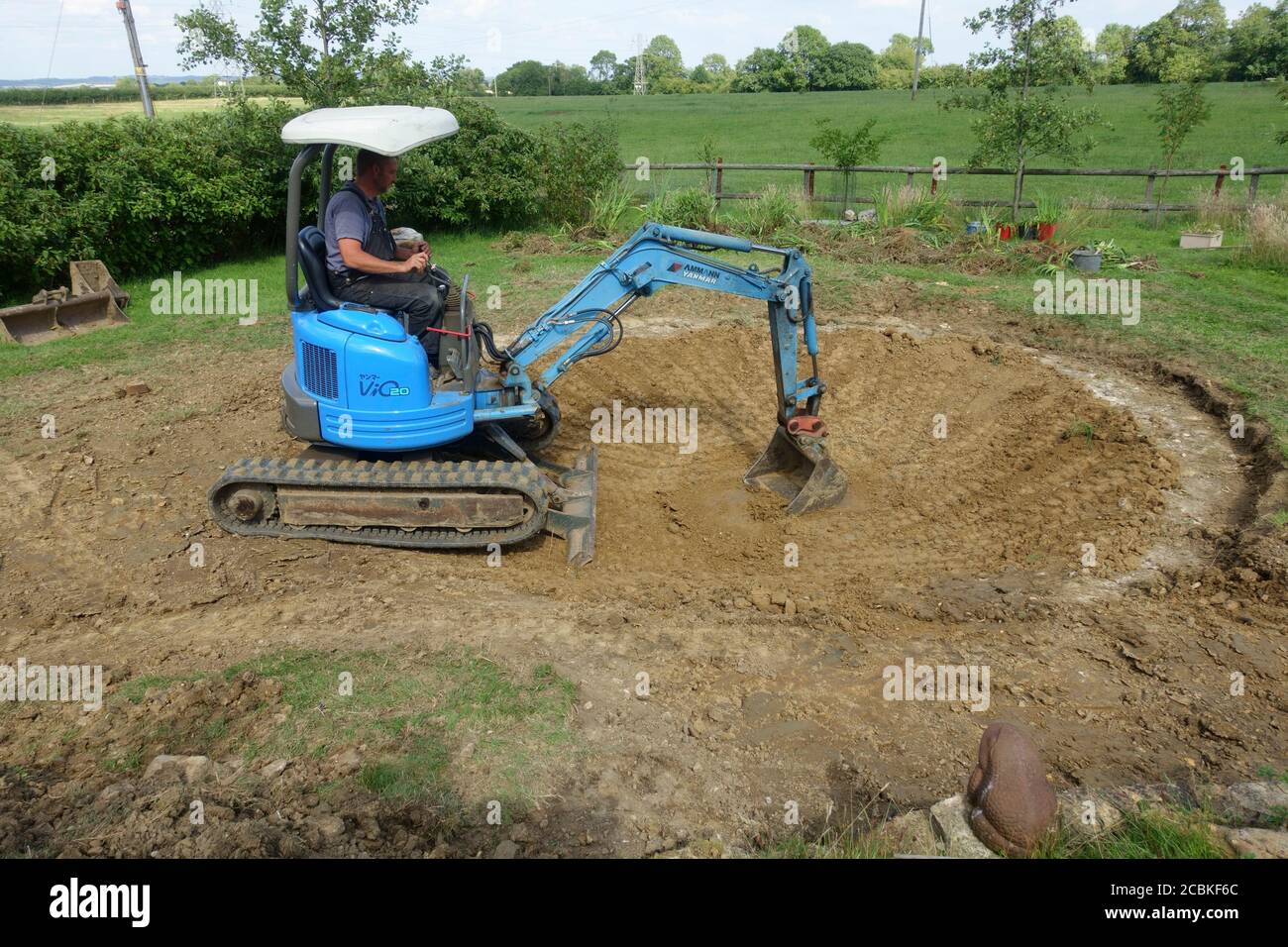 Workman in excavator removing soil to increase size of large pond in Cotswolds UK Stock Photo