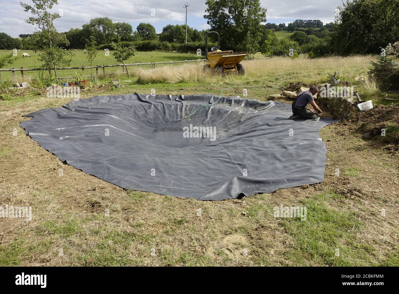 Workman installing EPDM rubber liner in new pond Cotswolds Stock Photo