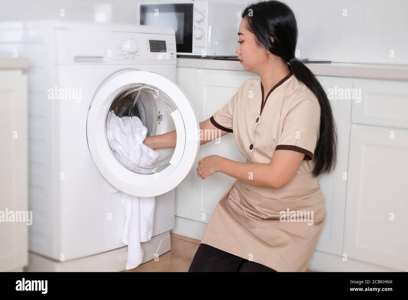 Young beautiful Asia maid loading the washing machine white clothing in hotel room Stock Photo