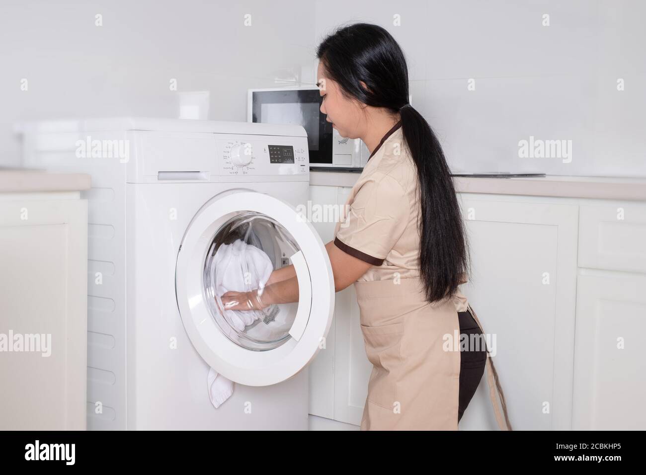 Young beautiful Asia maid loading the washing machine white clothing in