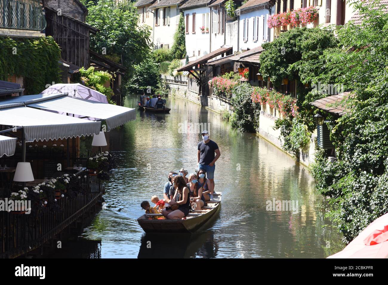 Group of people with mask on wooden boat with tourist guide  sailing  through romantic canal ,little Venice, a course of the Lauch in Colmar. Stock Photo