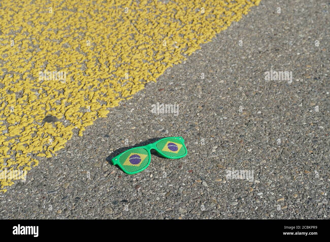 Kitschy broken sunglasses with printing applied color of Brazilian flag lying near yellow pedestrian crossing as symbol of Carnival in Rio de Janeiro. Stock Photo