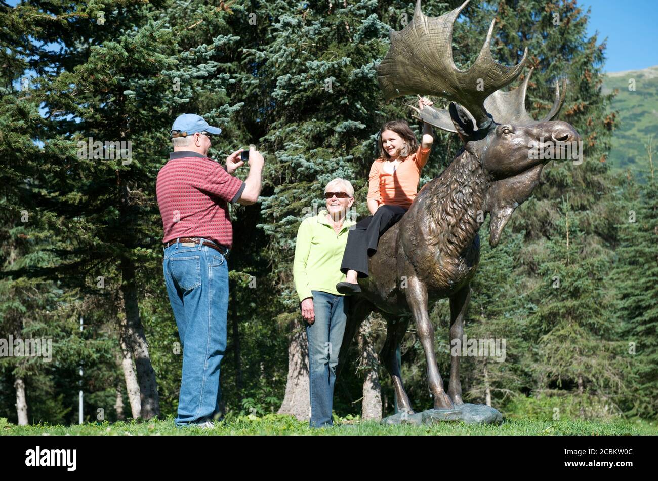 Grandparents photographing granddaughter with elk statue at Alyeska resort, Girdwood, Alaska, USA Stock Photo