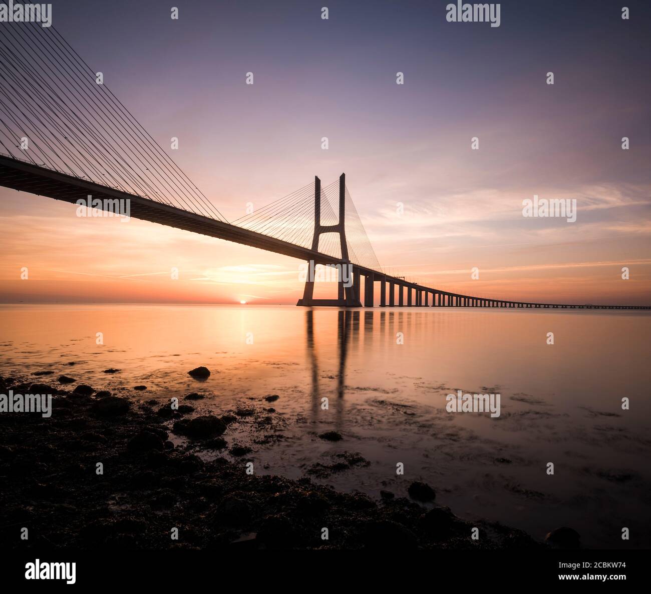 Silhouette of Vasco Da Gama Bridge against dramatic orange sky, Tagus River, Lisbon, Portugal Stock Photo
