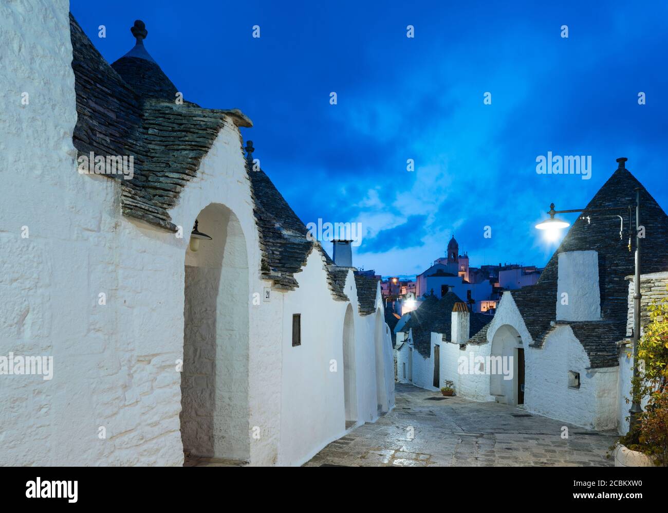 Paved alley and whitewashed trullo houses at dusk, Alberobello, Puglia, Italy Stock Photo