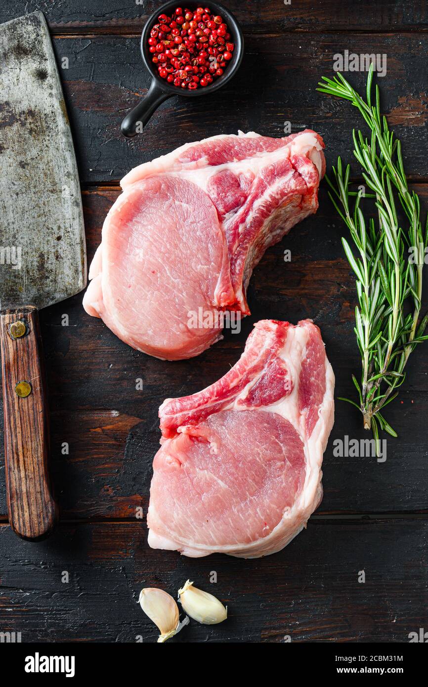 Organic bio Pork steaks, fillets for grilling, baking or frying, Fith butcher cleaver ower dark wood planks. Overhead view Stock Photo