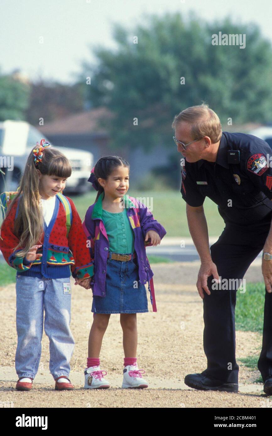 Austin, Texas USA, 1988: Hispanic and Anglo girls age 6 help male Anglo police officer in uniform by answering some questions while walking home from school.  Model Release. ©Bob Daemmrich Stock Photo