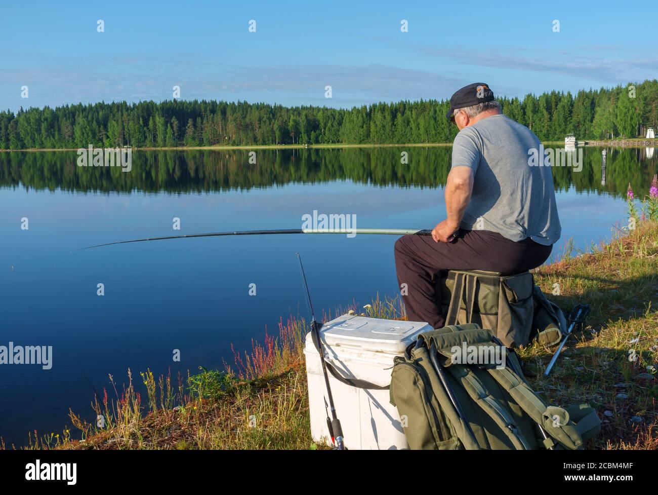 An elderly caucasian male angling from lake shore at Summer , Finland Stock Photo