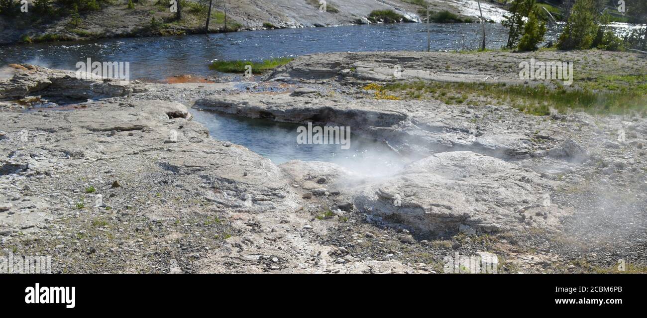 Late Spring in Yellowstone National Park: Spiteful Geyser & Fan Geyser of the Morning Glory Group on the Bank of Firehole River in Upper Geyser Basin Stock Photo