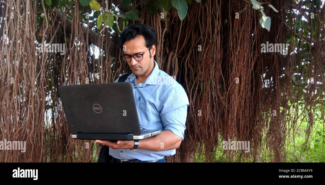 DISTRICT KATNI, INDIA - OCTOBER 23, 2019: An indian corporate smart boy working on laptop around natural tree root environment background. Stock Photo