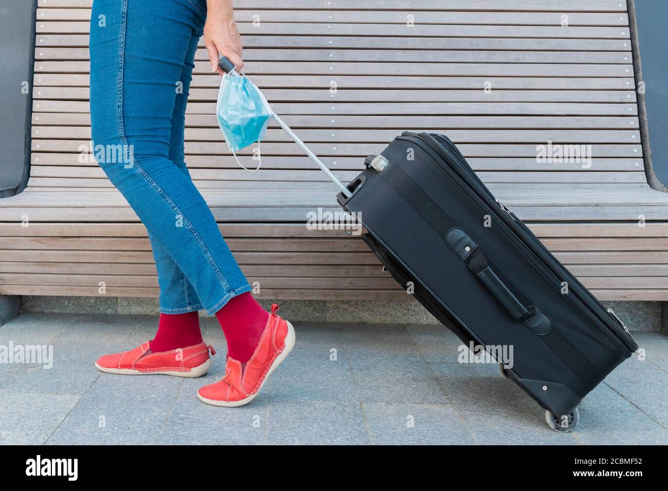 Cropped view of woman, holding suitcase and protective face mask. Traveler  holding medical mask in hand and moving luggage. Legs of woman, mask and ba  Stock Photo - Alamy