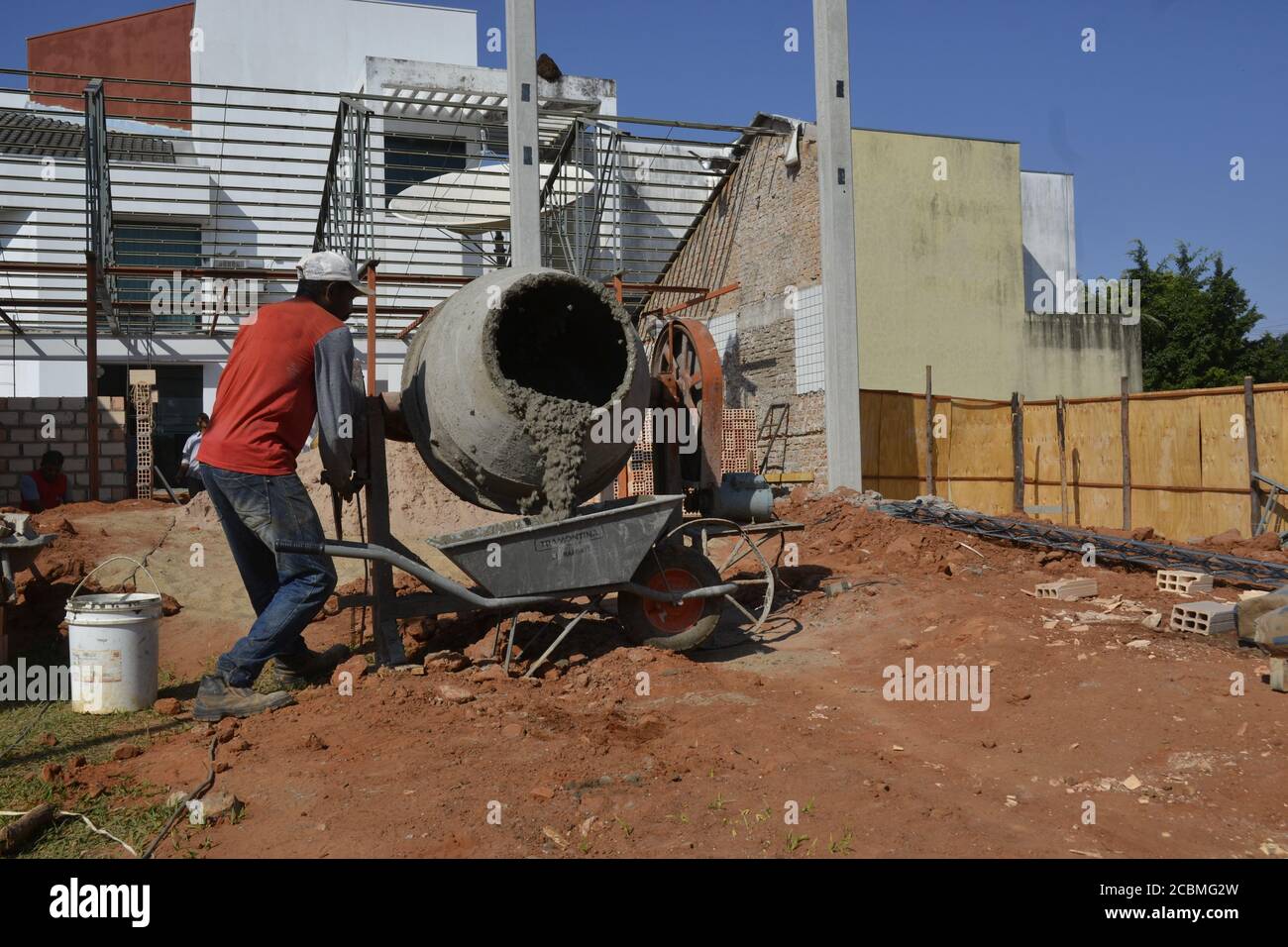 Man, worker in civil construction area, removing cement from mixer, for concrete under construction, in panoramic view Stock Photo