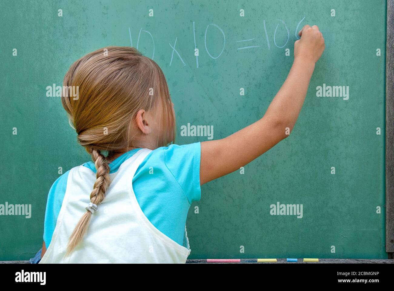 young girl writing math problem on retro green chalkboard Stock Photo