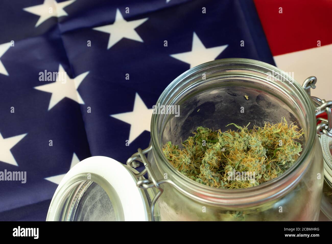 Big Glass Jar of Weed Buds with USA national flag background. Cannabis closeup with copy space