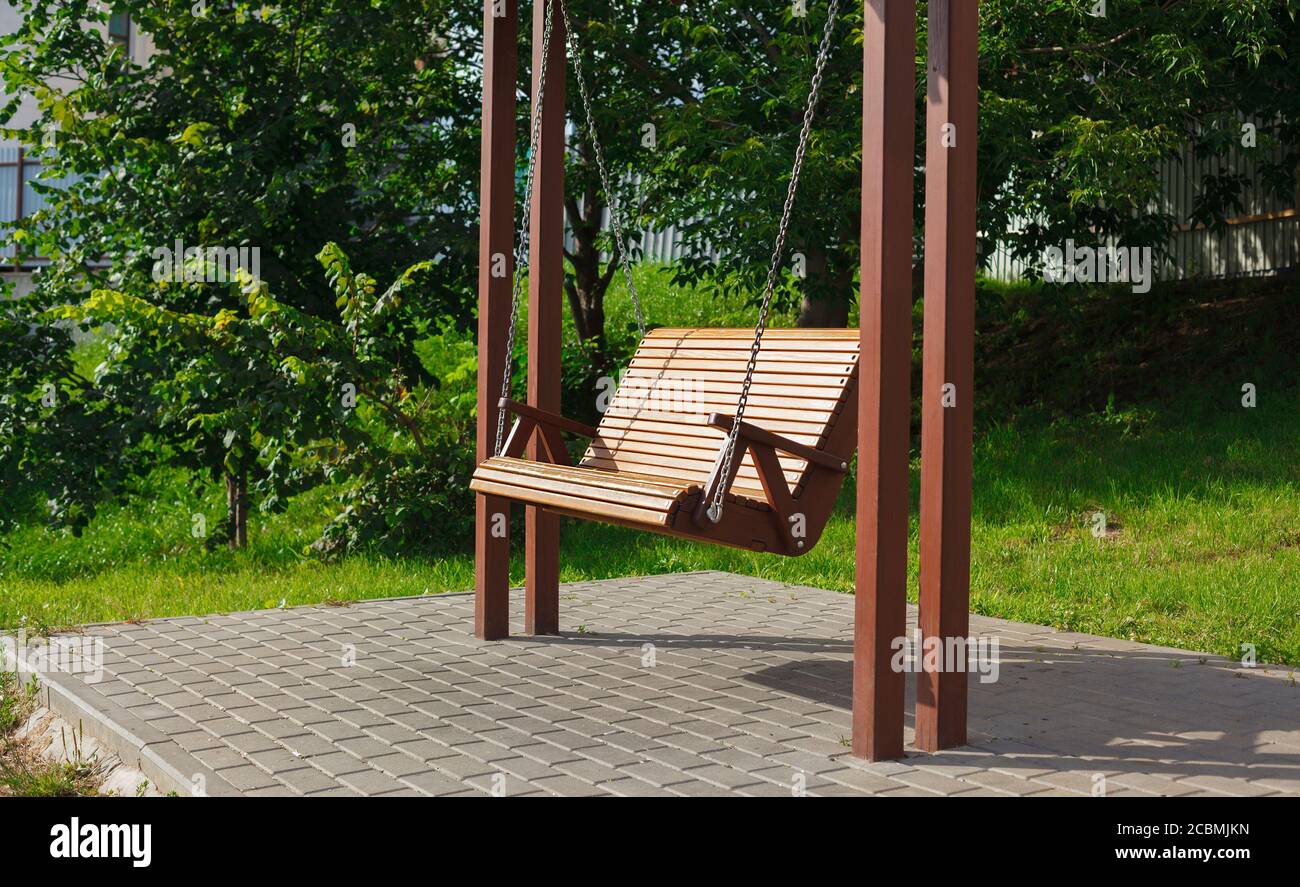 Wide wooden swing in the yard, swing for grown ups hanging on the chains, installation in country yard Stock Photo