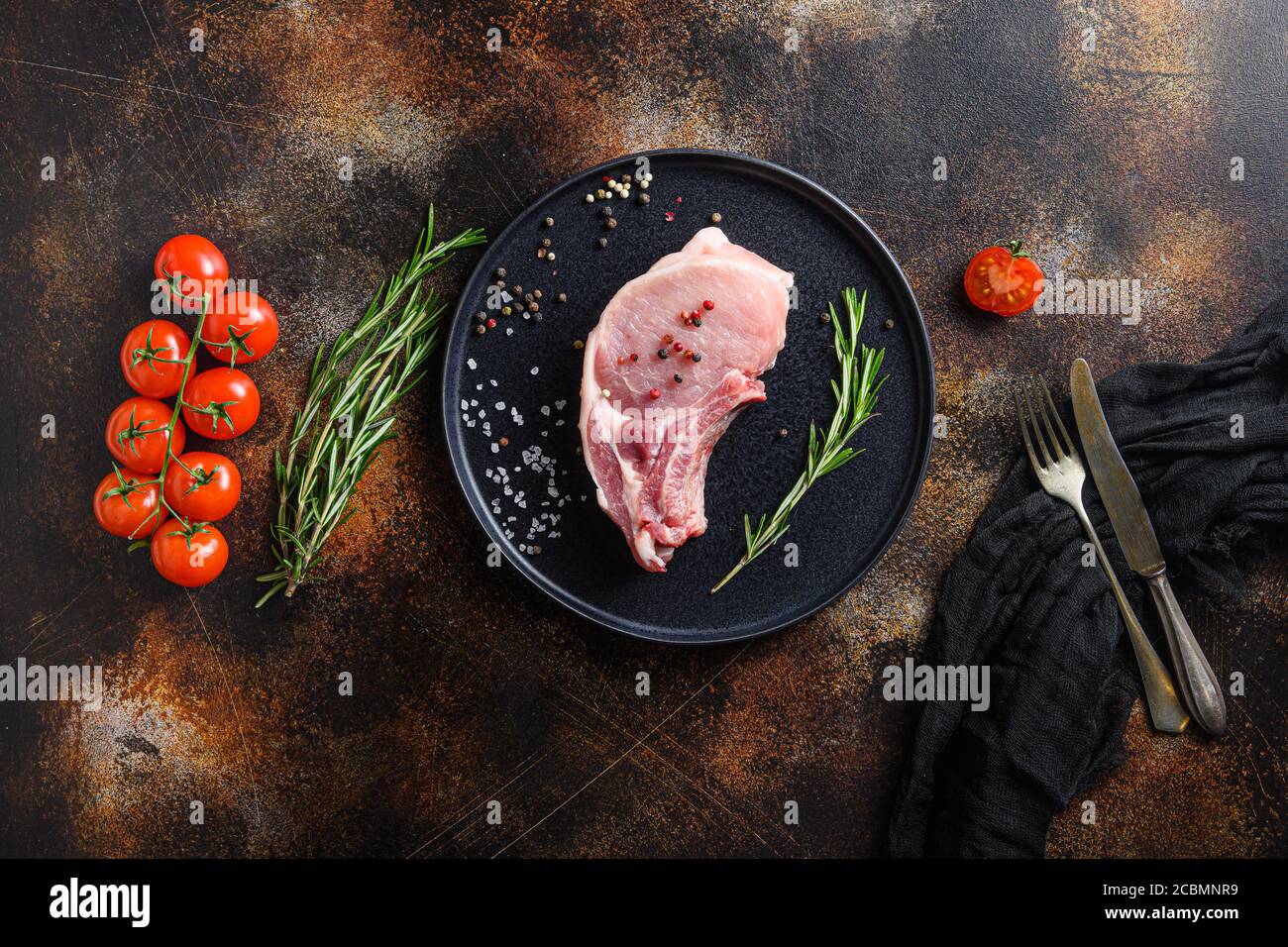 Pork belly Farm fresh , cutlet in round black modern plate on a old rustic dark metall surface rosemary garlic peppercorns top view space for text Stock Photo