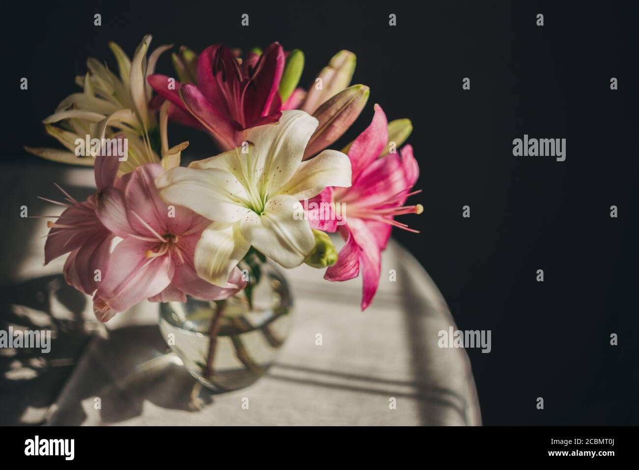 Romantic bouquet of the white and pink lilies in a glass vase on a dark ...