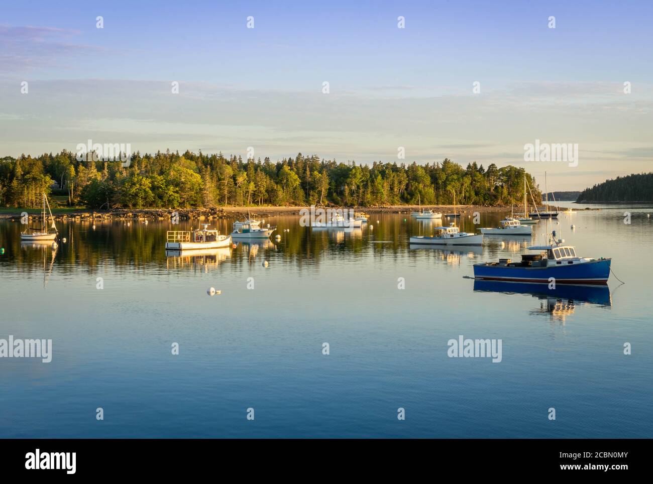 Sunset on a cove in Pretty Marsh in Maine.  Several boats sit anchoored in the water with the sun casting a golden light on them Stock Photo