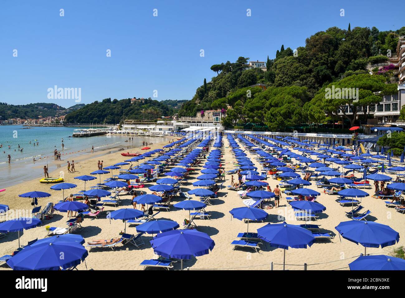 Elevated view of a sandy beach with rows of sun umbrellas, people swimming and sunbathing and the coast in the background, Lerici, La Spezia, Italy Stock Photo