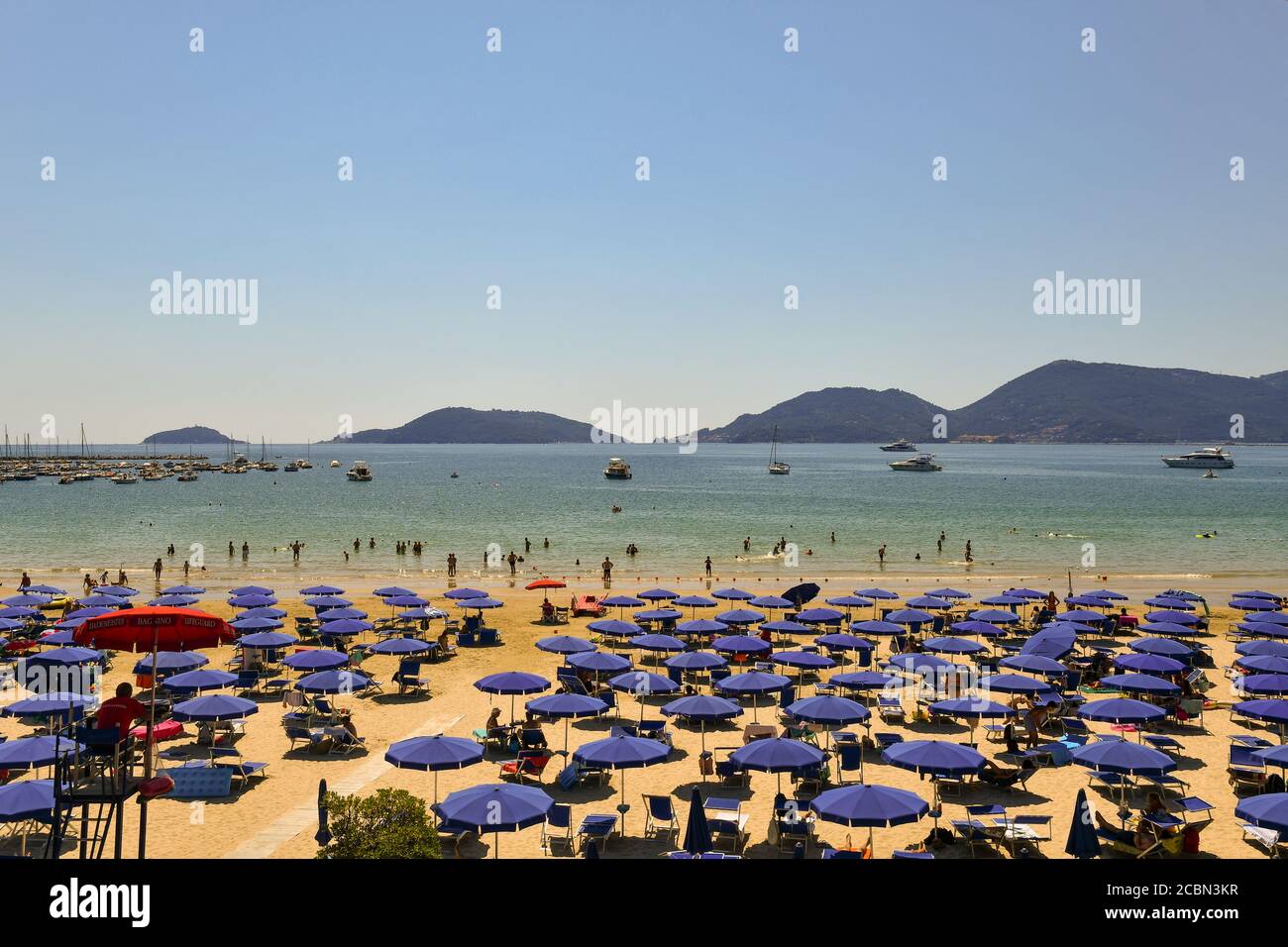 Scenic view of a sandy beach with rows of sun umbrellas, vacationers on the shore and the promontory of Porto Venere in summer, Lerici, Liguria, Italy Stock Photo