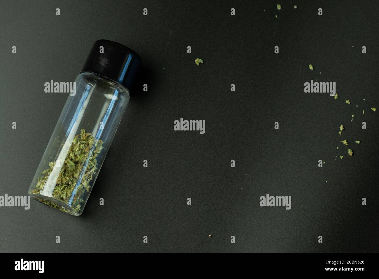 Top view of crumbled cannabis in little bottle on black background Stock Photo