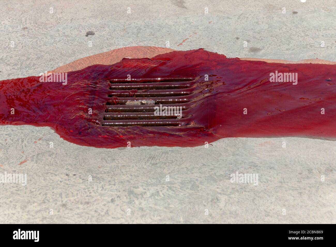 a close up view of red paint being washed down the drain on a main road Stock Photo