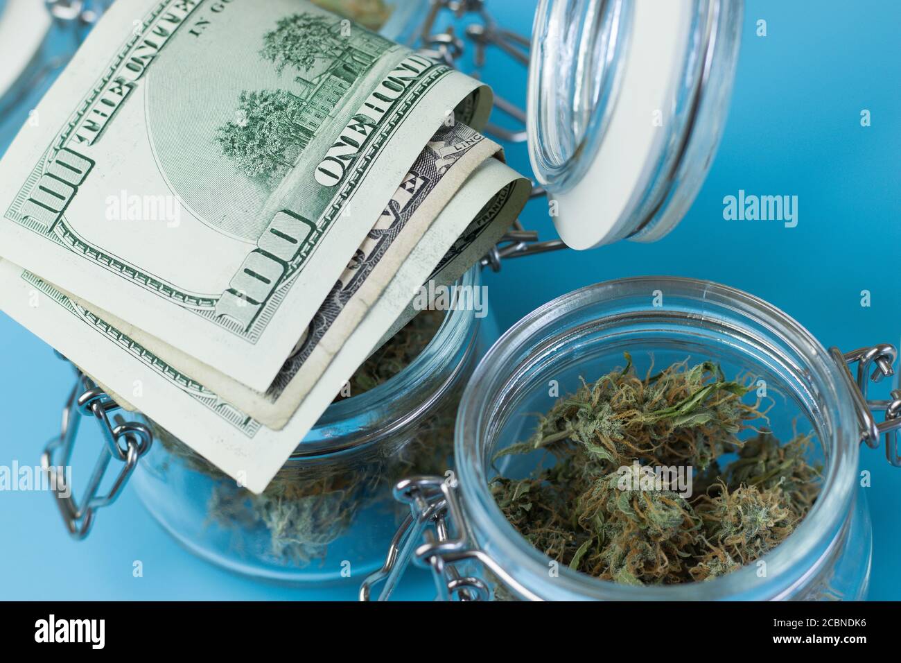 Buying marijuana product from legal shop. Cannabis buds in jar and money on blue background Stock Photo