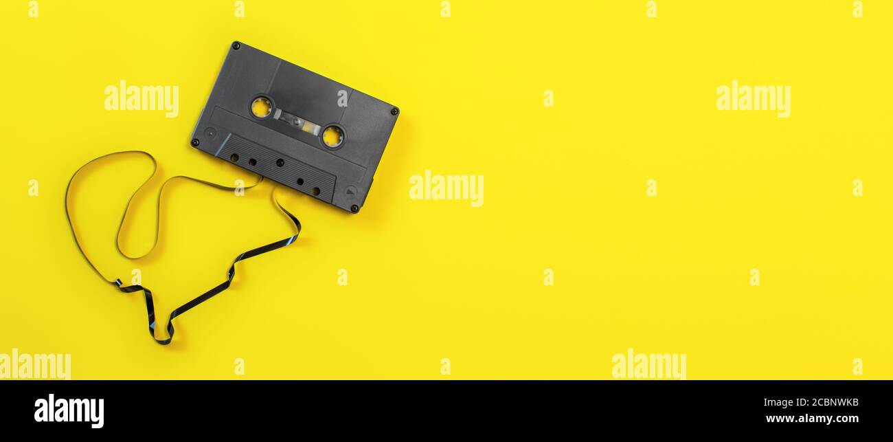 Overhead shot audio cassette with some tape out, on yellow board, wide banner space