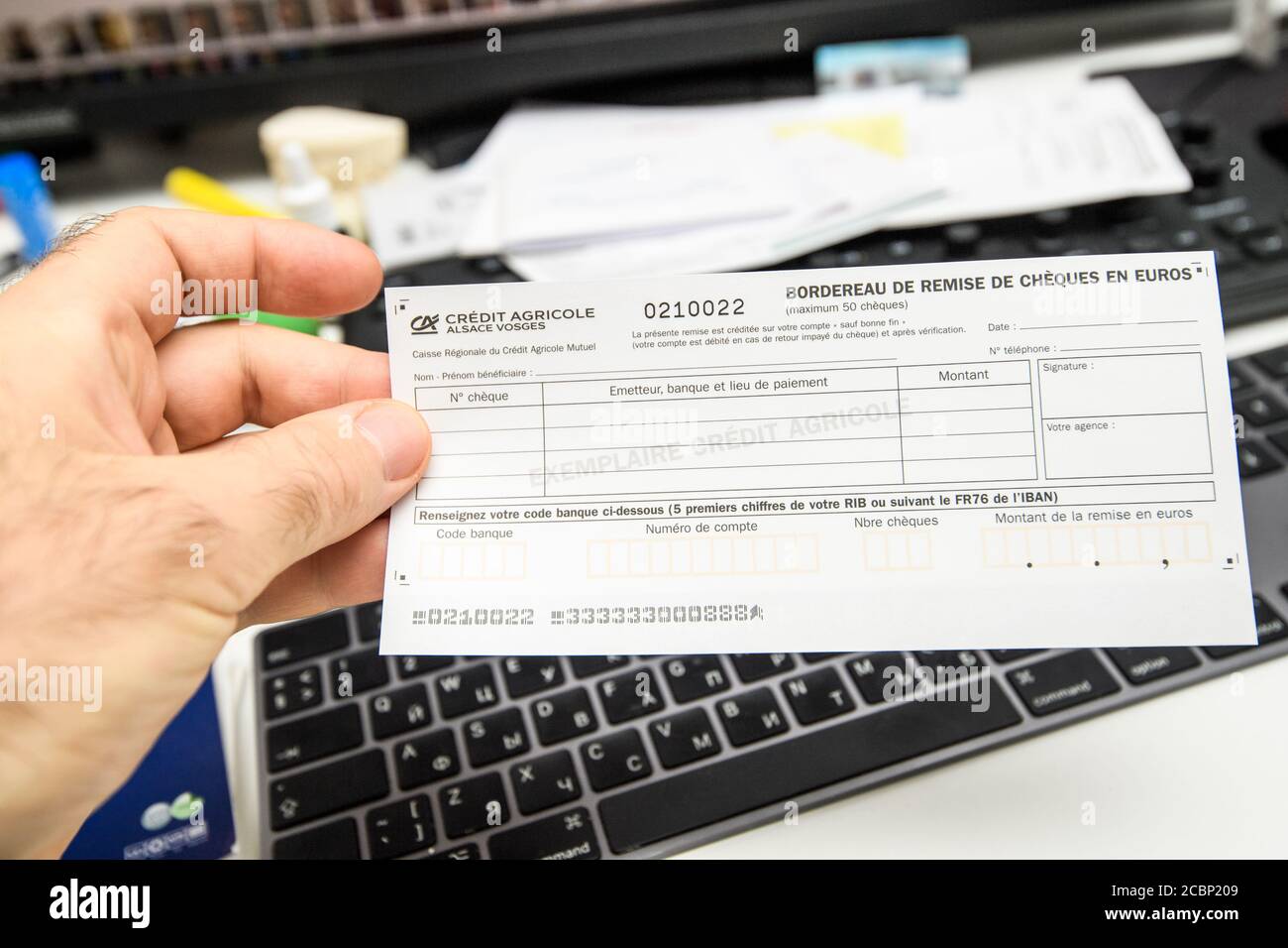 Paris, France - Nov 15, 2019: Man hand holding above computer keyboard Credit Agricole French bank remittance slip for checks in euros Stock Photo