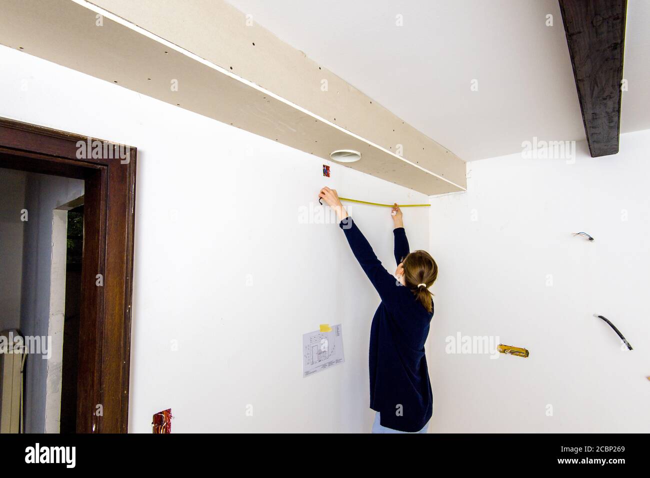 Side view of elegant woman architect measuring with yellow tape the length hole to the nearest wall reconfiguration of new placo plate construction in place. Stock Photo