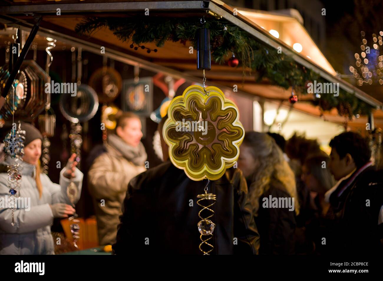 Hanging ornaments at a Christmas market stall, people busy behind, sun, wind spinner, wind chime,decorations for patios, street photography, authentic Stock Photo