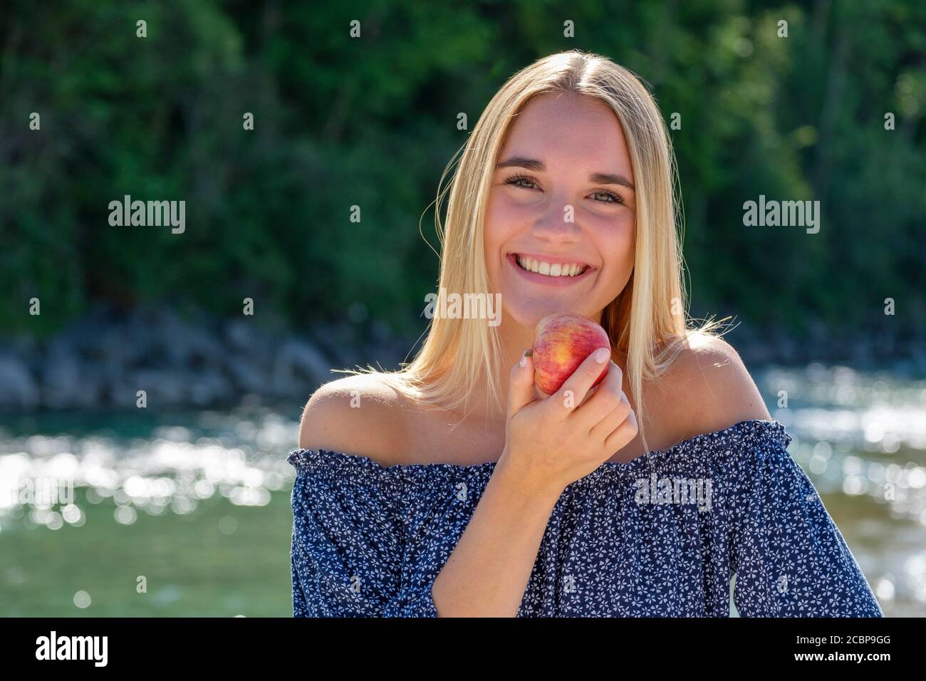 Portrait, young blonde woman laughing at the water, eating an apple