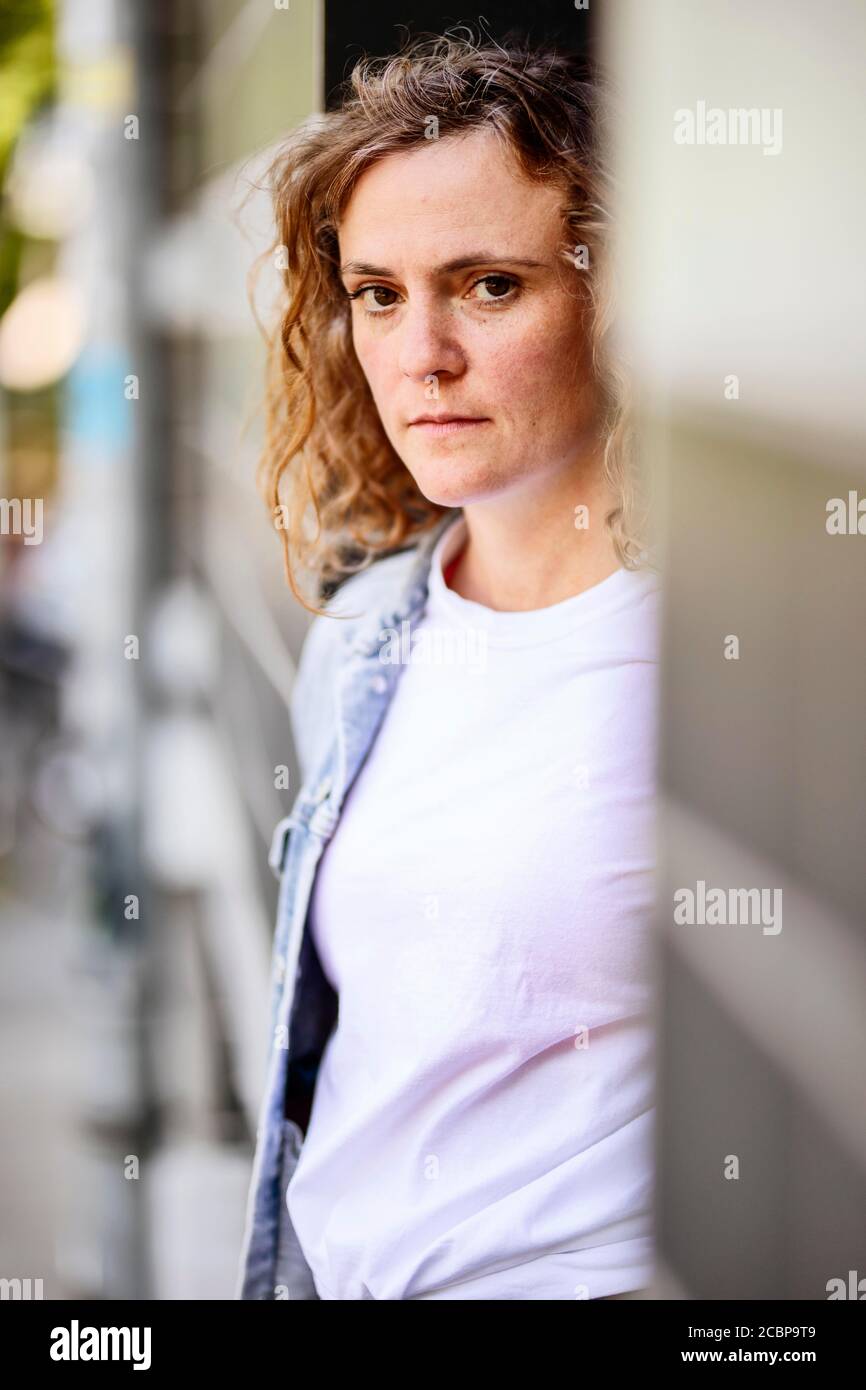 Young woman with wild curly hair looks serious, portrait in a house entrance, Cologne, North Rhine-Westphalia, Germany Stock Photo