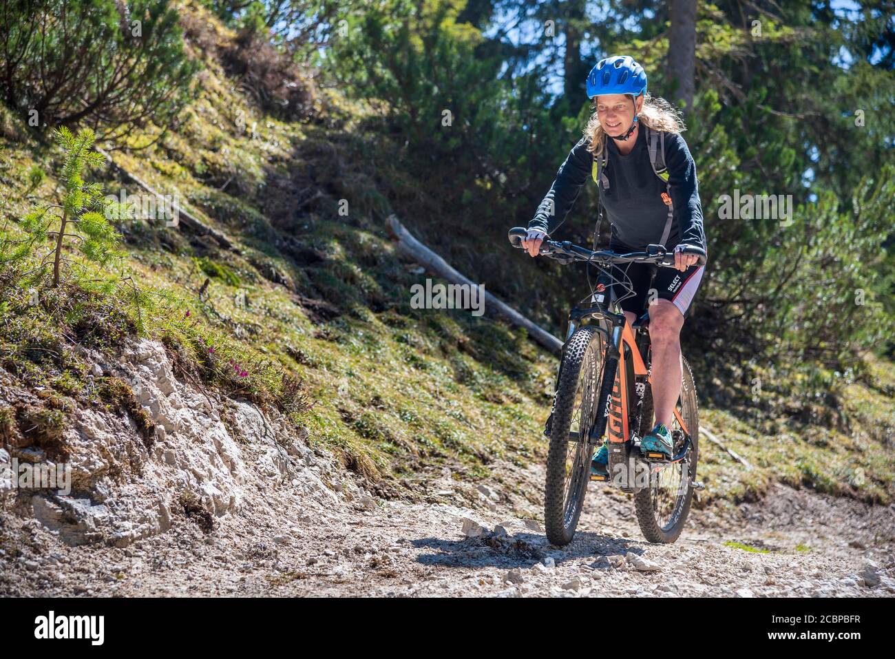 Female mountain biker rides with eMTB on a cart track uphill in the mountain forest, Rofan Mountains, Steinberg am Rofan, Tyrol, Austria Stock Photo