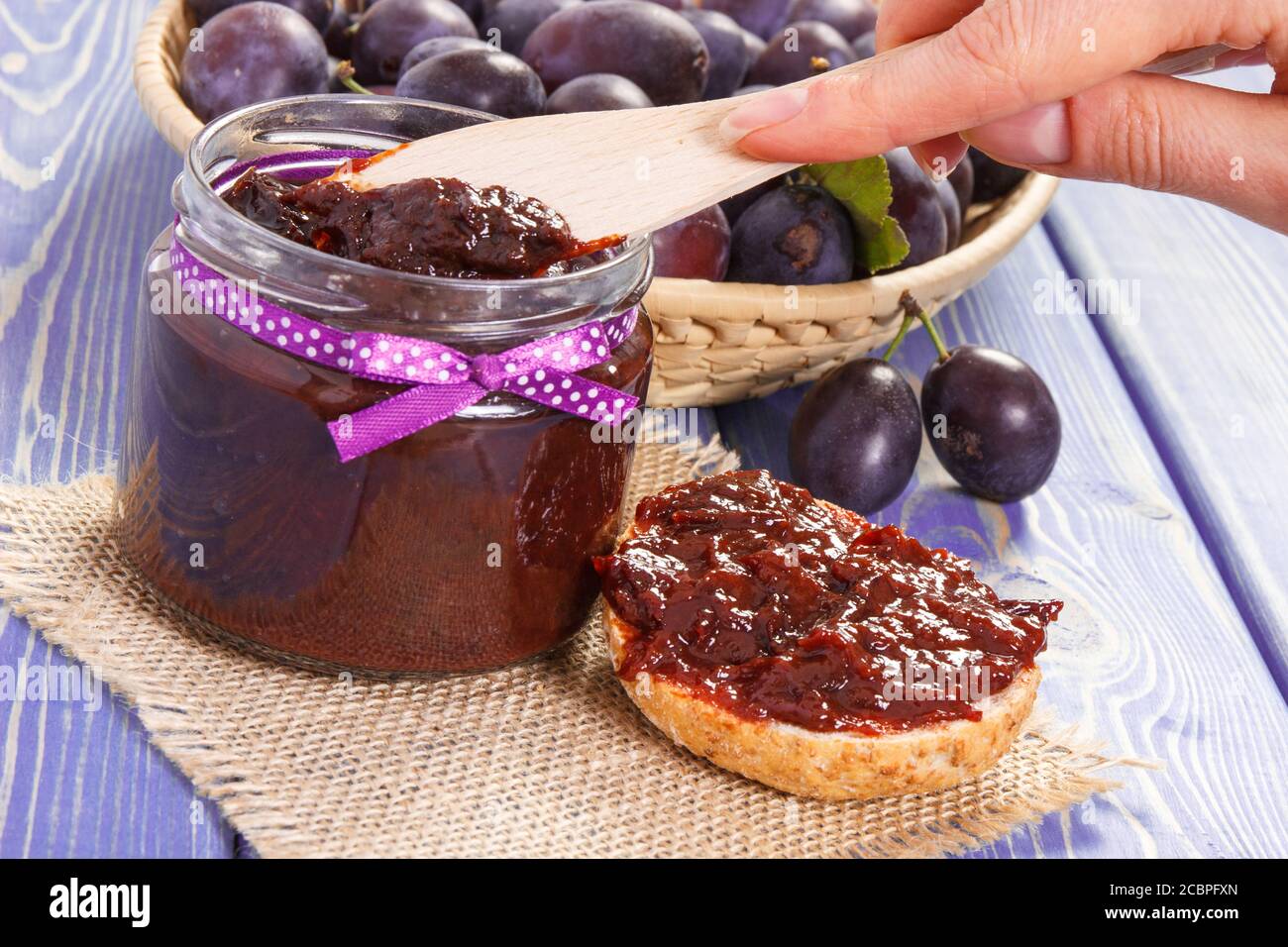 Hand of woman with wooden knife preparing sandwiches with plum marmalade or jam, concept of healthy sweet snack or dessert Stock Photo