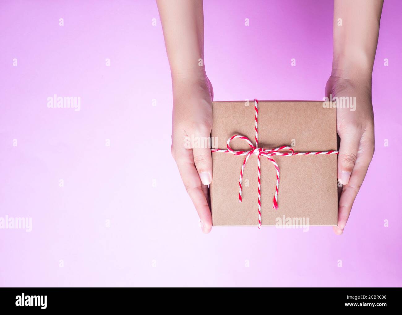 Girl's hands holding the simply package box as a present for Christmas, new year, valentine day or anniversary on pink background, top view Stock Photo