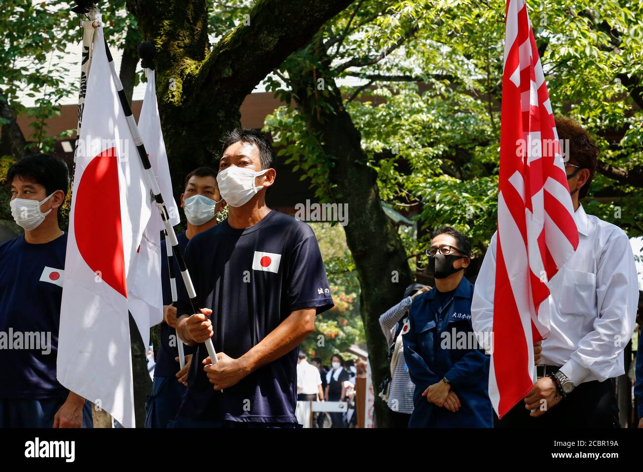 Tokyo, Japan. 15th Aug, 2020. Japanese nationalists wearing face masks hold war flags of the Imperial Japanese Army during the 75th anniversary of Japan's surrender in World War II at Yasukuni Shrine. This year, the temple has set signboards promoting the social distancing to prevent the spreading of the new coronavirus (COVID-19) disease at the Yasukuni Shrine. Credit: Rodrigo Reyes Marin/ZUMA Wire/Alamy Live News Stock Photo